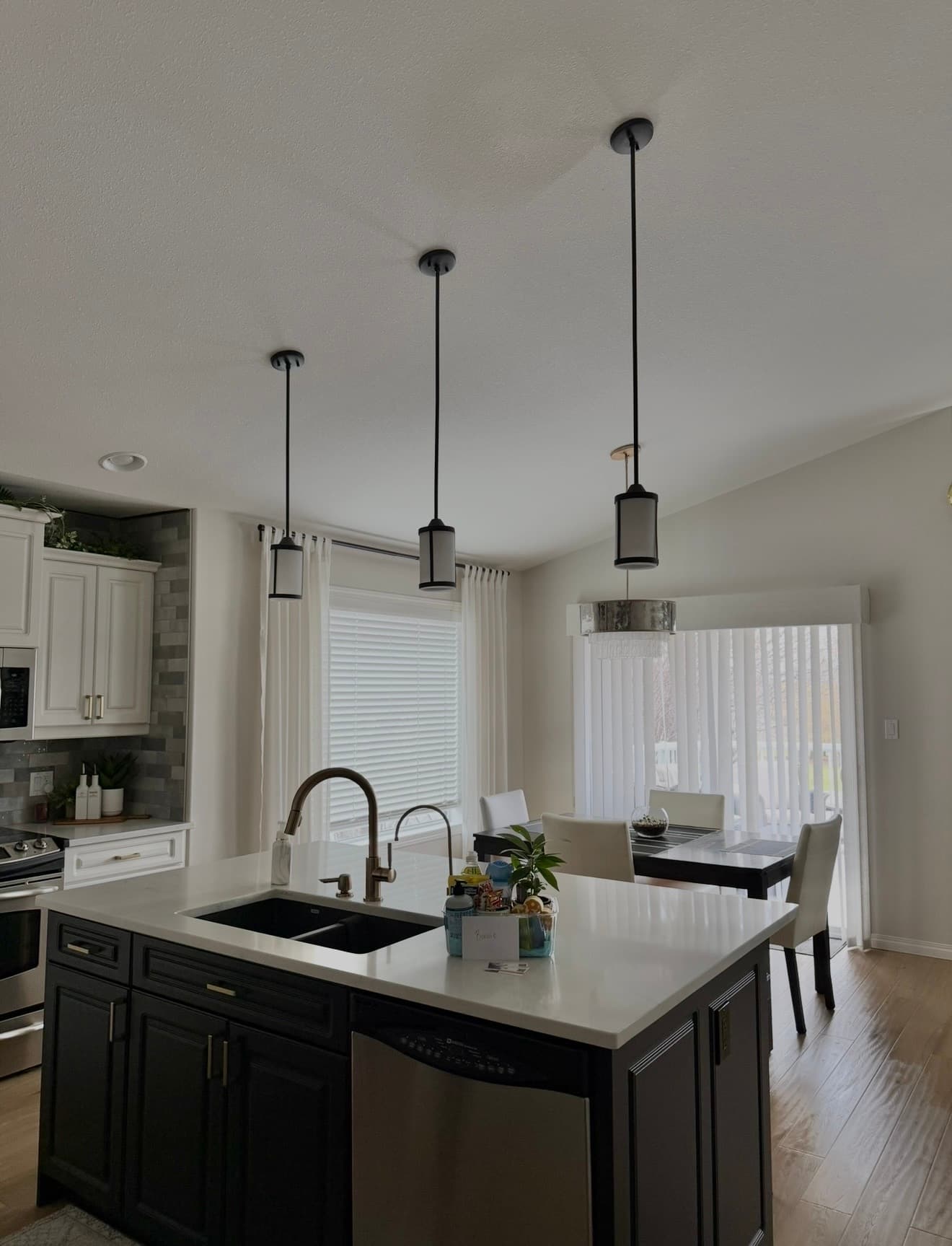 Modern kitchen featuring a dark island with white countertops, three pendant lights, and a dining area.